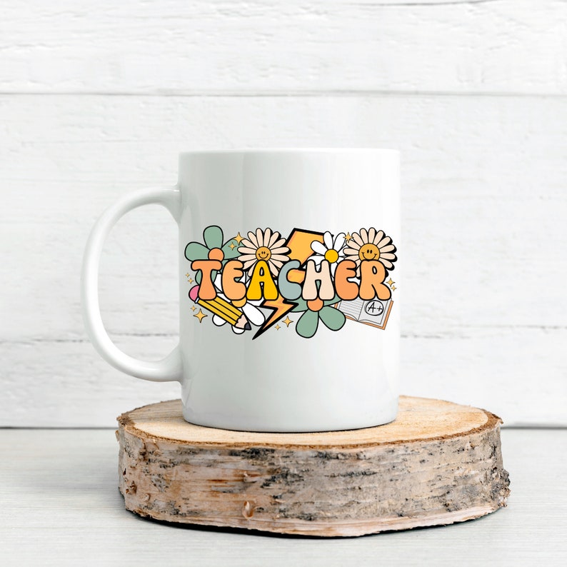 May include: White ceramic mug with a colorful graphic of the word "TEACHER" in a retro font, surrounded by flowers, a pencil, a lightning bolt, and a book with an A+ grade.