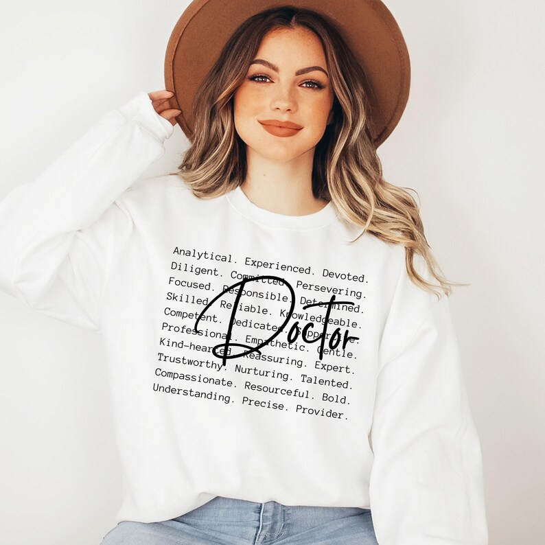May include: White sweatshirt with the word "Doctor" written in black cursive lettering. The sweatshirt has a list of positive adjectives describing a doctor printed in black text.