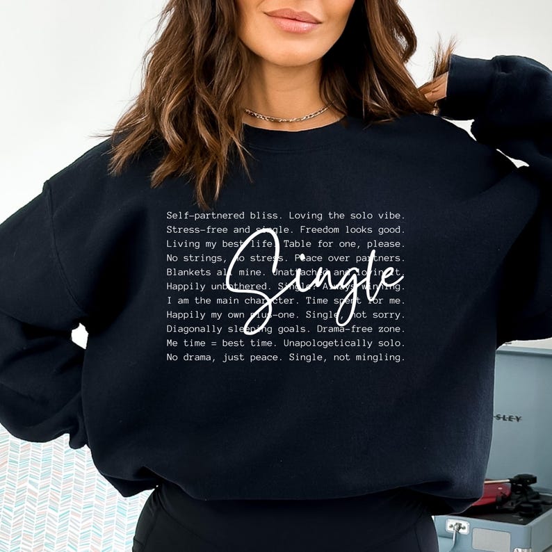May include: Black sweatshirt with white text that reads "Self-partnered bliss. Loving the solo vibe. Stress-free and single. Freedom looks good. Living my best life. Table for one, please. No strings, no stress. Peace over partners. Blankets all mine. Unattached and thriving. Happily unbothered. Single, not sorry. I am the main character. Time spent for me. Happily my own u-one. Single, not sorry. Diagonally sleeping goals. Drama-free zone. Me time = best time. Unapologetically solo. No drama, just peace. Single, not mingling."