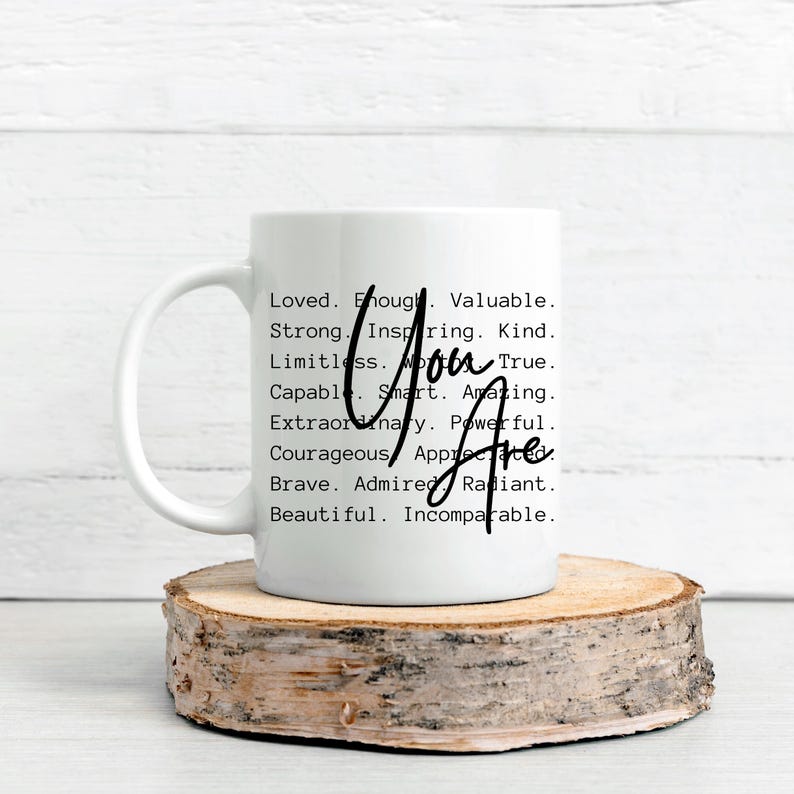 May include: White ceramic mug with a black handle. The mug has a black text design that reads "You Are" and lists positive attributes such as "Loved, Enough, Valuable, Strong, Inspiring, Kind, Limitless, True, Capable, Smart, Amazing, Extraordinary, Powerful, Courageous, Appreciated, Brave, Admired, Radiant, Beautiful, Incomparable."