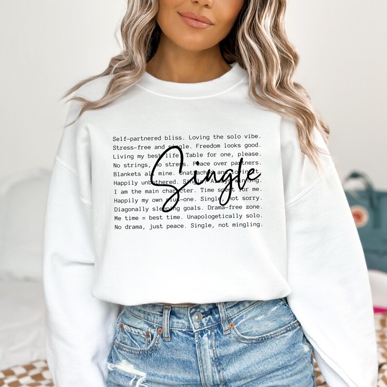 May include: White sweatshirt with black text that reads "Self-partnered bliss. Loving the solo vibe. Stress-free and single. Freedom looks good. Living my best life. Table for one, please. No strings, no stress. Peace over partners. Blankets all mine. Unattached and thriving. Happily untethered. Single. I am the main character. Time spent on me. Happily my own u-one. Single, not sorry. Diagonally sleeping goals. Drama-free zone. Me time = best time. Unapologetically solo. No drama, just peace. Single, not mingling."