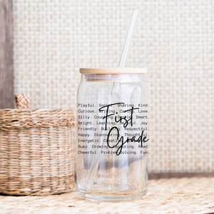 May include: A clear glass tumbler with a bamboo lid and a straw. The words "First Grade" are written in a script font, surrounded by descriptive words like "Playful" and "Curious". A woven basket is in the background.
