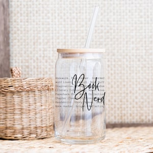 May include: A clear glass tumbler with a bamboo lid and a straw. The tumbler has a black graphic that reads "Bookworm. Page Turner. Informed. Word Lover. Novelist. Book Buff. Imaginative. Thought. Wisdom. Book Nerd. Literary Enthusiast. Novel Love. Paperback Pro. Shelf Collection. Chapter Chase. Fiction. Readholic. Story Seeker. Smart. Book Hunter. Bright. Reflecting."