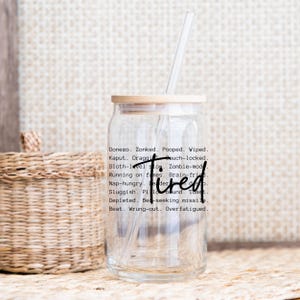 May include: A clear glass tumbler with a bamboo lid and a black straw. The tumbler has a black graphic that reads "Donezo. Zonked. Pooped. Wiped. Kaput. Draggi Gouch-locked. Sloth-level slow. Zombie-mod Running on fumes. Brain-fried Nap-hungry. De der Tired Sluggish. Pilo bound. Toast. Depleted. Bed-seeking missile Beat. Wrung-out. Overfatigued."