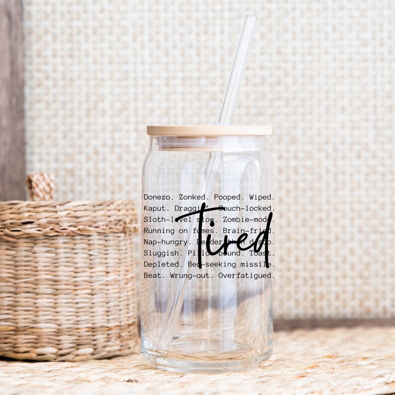 May include: A clear glass tumbler with a bamboo lid and a black straw. The tumbler has a black graphic that reads "Donezo. Zonked. Pooped. Wiped. Kaput. Draggi Gouch-locked. Sloth-level slow. Zombie-mod Running on fumes. Brain-fried Nap-hungry. De der Tired Sluggish. Pilo bound. Toast. Depleted. Bed-seeking missile Beat. Wrung-out. Overfatigued."