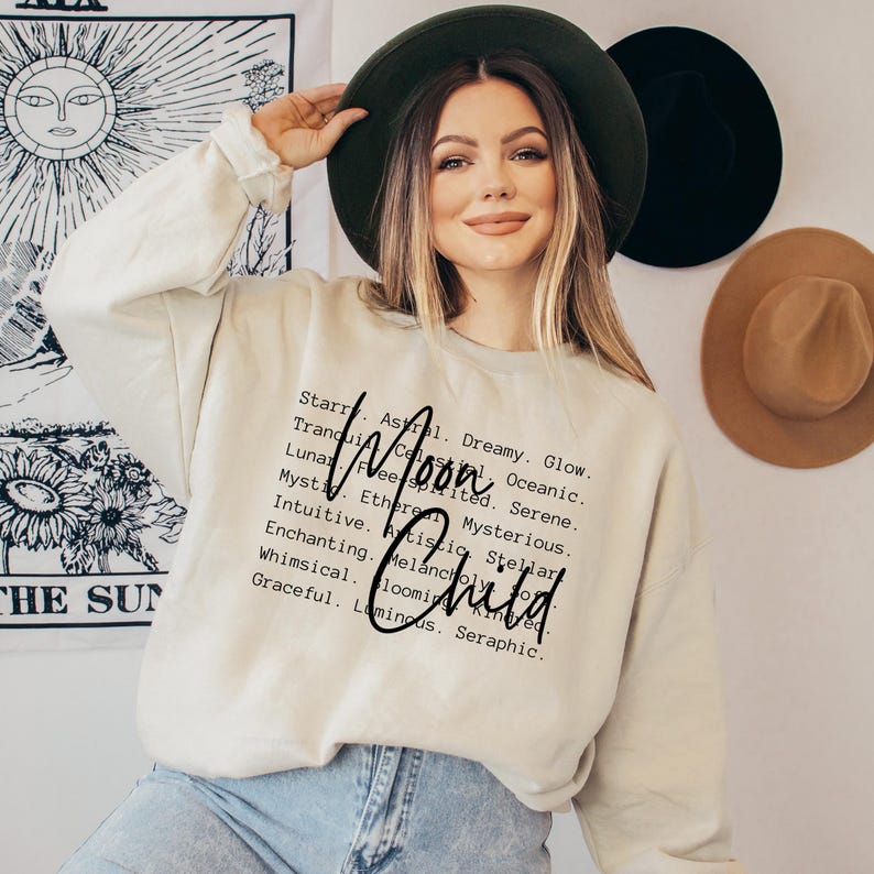 May include: A cream-coloured sweatshirt with the text "Moon Child" in black lettering. The text is surrounded by a list of words describing the moon, such as "dreamy", "glow", "serene", and "ethereal".