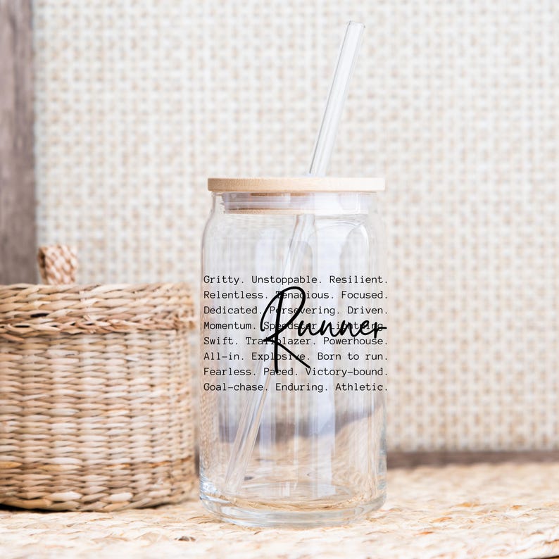 May include: A clear glass water bottle with a bamboo lid and a black straw. The bottle has a motivational quote printed on it that reads: "Gritty. Unstoppable. Resilient. Relentless. Tenacious. Focused. Dedicated. Persovering. Driven. Momentum. Trailblazer. Powerhouse. Runner. All-in. Explosive. Born to run. Fearless. Paced. Victory-bound. Goal-chase. Enduring. Athletic."