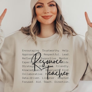 Può includere: Una felpa girocollo beige con testo nero che elenca vari tratti professionali tra cui Encouraging, Trustworthy, Help, Approachable, Respectful, Lead, Reflective, Supportive, Mentor, Experienced, Insightful, Guide, Strategic, Organized, Friendly, Knowledgeable, Observant, Kind, Collaborative, Patient, Caring, Data-driven, Listener, Adapted, Focused, Aid, Teach, Direction, e le parole Resource Teacher in un grande carattere corsivo.