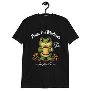 May include: Black t-shirt with a cartoon frog holding a coffee mug. The frog is green with a yellow belly and is surrounded by flowers and a mushroom. Text on the shirt reads "From The Windows To The Walls - I'm About To".