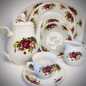 Può includere: Un set da tè bianco con un motivo a rose. Il set comprende una teiera, una lattiera, una zuccheriera, una tazza e un piattino.