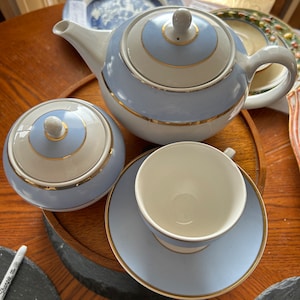 Può includere: Un set da tè blu e bianco con finiture dorate. Il set comprende una teiera, una zuccheriera e una tazza da tè con piattino.