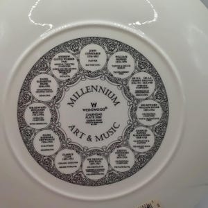 Könnte beinhalten: Weiße Keramikplatte mit einem schwarz-weißen Design mit dem Text "Millennium Art & Music" und den Namen von Künstlern und Komponisten. Die Platte ist eine Kalenderplatte von Wedgwood, hergestellt in England.