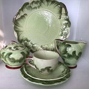 May include: A green and white tea set with a floral design. The set includes a teapot, sugar bowl, creamer, cup and saucer, and a serving plate.
