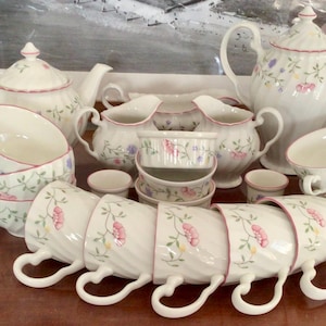 May include: A set of white teacups and saucers with floral designs in pink, blue, and green. The set includes a teapot, creamer, sugar bowl, and a variety of cups and saucers.