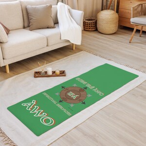 May include: A green yoga mat with white text that reads "AWO" and "Spiritual Services". The mat also features a circular design with the text "IFA" and arrows. The mat is rectangular and is on a white rug.