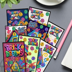 May include: A collection of colorful cards with house illustrations and text like "Drippin' Home Goals" and "Brick Dreams." Each card features numbered circles. A pink pencil, a cup of coffee, and a succulent plant are also visible.