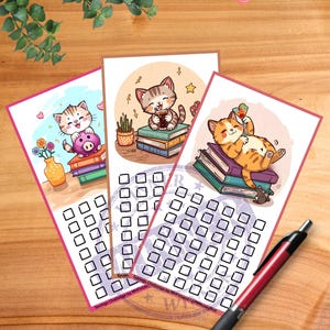 May include: Three illustrated savings challenge trackers featuring cartoon cats. Each card has a different cat illustration, with a series of blank squares for tracking savings. A red pen rests on the wooden surface.