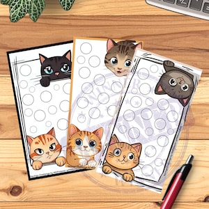 May include: Four cat-themed savings challenge trackers with various cat illustrations. Each tracker has a different cat design, with a series of circles for tracking savings. A calculator and pen are also visible.