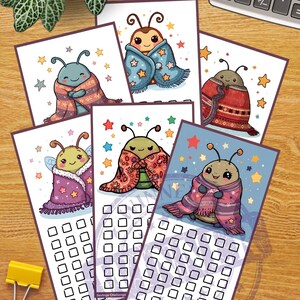 May include: A collection of colorful savings challenge cards featuring cartoonish bugs wrapped in blankets. Each card has a different bug design and a grid of boxes for tracking savings. The cards are decorated with stars and other whimsical elements.
