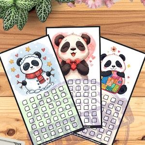 May include: Three illustrated savings challenge cards featuring pandas. One panda is a snowman, another holds a heart, and the third is wrapped in a blanket. Each card has a grid of squares for tracking savings. The cards are on a wooden surface with a hundred-dollar bill.