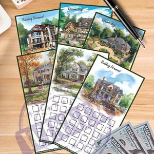 Może przedstawiać: Karty z ilustracjami domów i frazami „Building Dreams!” i „Dream Big!” są ułożone na drewnianej powierzchni. Czarny długopis i kilka banknotów 100-dolarowych są również obecne. Karty mają siatkę wyzwań oszczędnościowych.