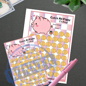 May include: Two "Catch All Piggy Challenge" savings trackers with a pink pen and two $100 bills. The trackers feature a pink piggy bank graphic and coin icons. The text "Catch All Piggy Challenge" is visible on the trackers.