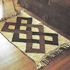 May include: A rectangular rug with a geometric pattern in shades of brown and cream. The rug features a repeating interlocking design and fringe along the edges. The rug is placed on a wooden floor.