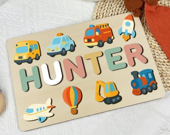 May include: Wooden puzzle with the name "HUNTER" in colorful letters. The puzzle features various vehicle shapes, including a bus, car, fire truck, rocket, airplane, hot air balloon, excavator, and train. The puzzle is designed for children.
