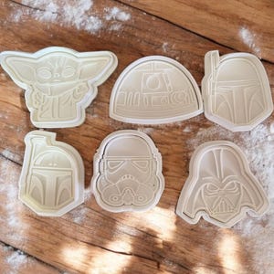 May include: Set of six white plastic cookie cutters featuring Star Wars characters: Yoda, R2-D2, Boba Fett, Darth Vader, Stormtrooper, and a Mandalorian.