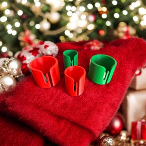 May include: Four Christmas gift tag cutters, two red and two green, on a red fuzzy surface. The cutters are made of plastic and have a small blade to cut through ribbon or string.