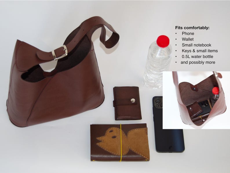 May include: A brown leather shoulder bag with a silver buckle, a wallet, a phone, and a wallet with a bird design. A water bottle is also present. The bag fits a phone, wallet, small notebook, keys, and a 0.5L water bottle.