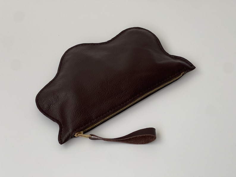 May include: A brown leather cloud-shaped clutch with a gold zipper and a brown leather strap.