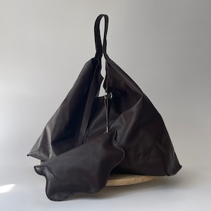 May include: A large brown leather tote bag with a single strap. The bag is folded over and has a small brown leather pouch attached to the front.