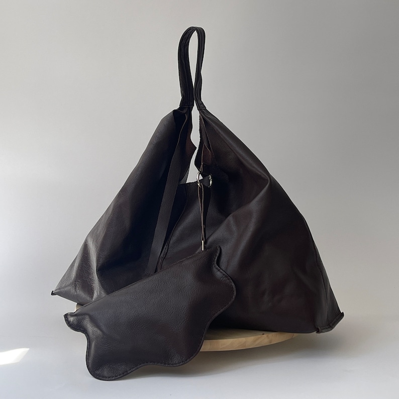 May include: A large brown leather tote bag with a single strap. The bag is folded over and has a small brown leather pouch attached to the front.