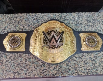May include: A gold and black WWE World Championship belt. The center plate features the WWE logo and the words "WORLD CHAMPION". The side plates also have the WWE logo. The belt is made of gold-colored metal and black leather.