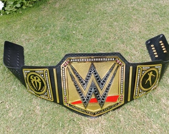 May include: A black and gold WWE Undisputed Championship belt. The center plate features a large gold "W" logo with red accents. The belt has the words "UNDISPUTED CHAMPION" and the Roman Reigns logo.