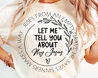 May include: Cream-colored t-shirt with the text "Let Me Tell You About My Jesus" in a circular design. The design includes floral elements and a heart symbol. The shirt is a casual wear item.