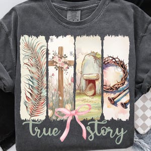 May include: A charcoal grey t-shirt with a watercolor design of a palm branch, a cross with flowers, a stone tomb, a crown of thorns, and nails. The text "true story" is printed below the design.