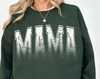 Könnte beinhalten: Ein dunkelgrüner Pullover mit dem Wort "MAMA" in Weiß bedruckt, mit einem abgenutzten, verblassten Effekt.