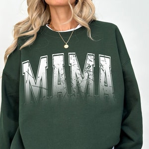 May include: A dark green sweatshirt with the word "MAMA" printed in white with a distressed, faded effect.