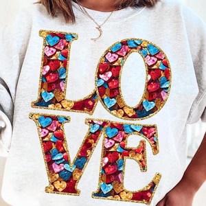 May include: A white sweatshirt with the word "LOVE" printed on the front. The letters are made up of small, colourful hearts with gold glitter accents.
