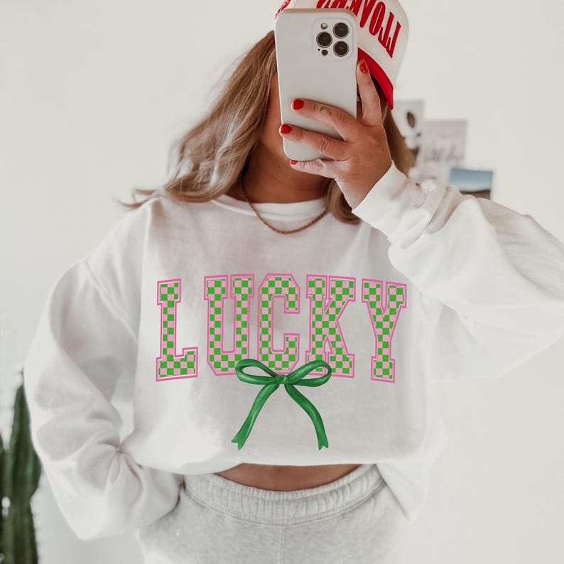 May include: White sweatshirt with a pink and green checkered "LUCKY" graphic with a green bow.