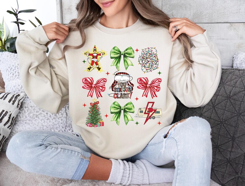 May include: Beige sweatshirt with a Christmas-themed design. The design includes images of a Santa Claus, bows, a Christmas tree, and a camper with a lightning bolt. The text on the sweatshirt reads "You Serious Clark?"