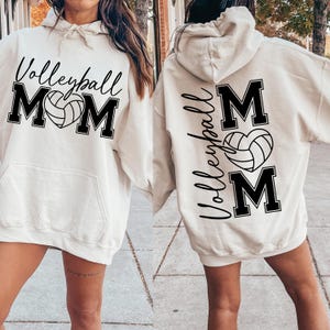 May include: A white hoodie with a black volleyball and the word "Volleyball Mom" printed on the front. The back of the hoodie has the words "Volleyball Mom" printed vertically with a volleyball in a heart shape.
