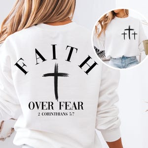 May include: White sweatshirt with the words "FAITH OVER FEAR" and a cross printed on the back. The text "2 CORINTHIANS 5:7" is printed below the cross. A white sweatshirt with three crosses printed on the front is also shown.