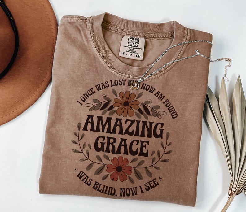 May include: A brown t-shirt with a floral design and the text "I once was lost but now am found Amazing Grace Was blind, now I see".