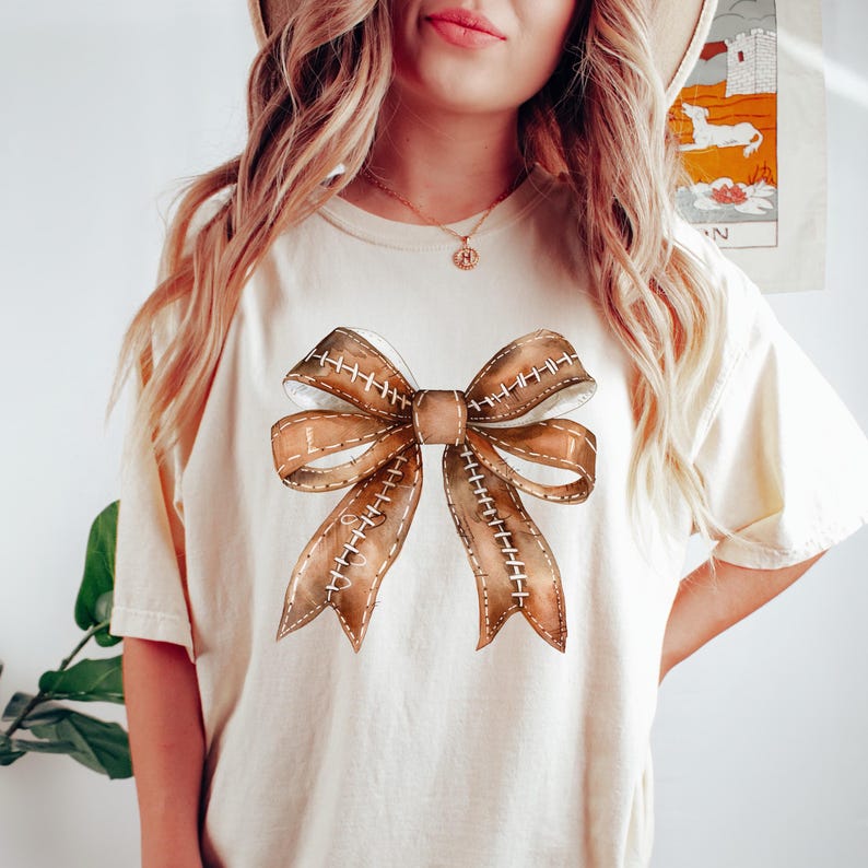 Pu&ograve; includere: T-shirt color crema con un design a fiocco ad acquerello. Il fiocco &egrave; marrone con dettagli di cucitura bianchi, creando un aspetto strutturato. La maglietta ha una vestibilit&agrave; rilassata, adatta per l'abbigliamento casual. Il design del fiocco &egrave; centrato sul davanti.