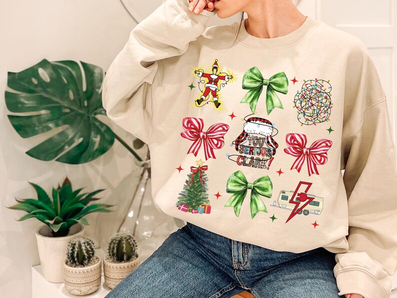 May include: Beige sweatshirt featuring Christmas-themed graphics. The design includes a Santa Claus figure, green and red bows, a Christmas tree, string lights, and the phrase "You Serious Clark!".