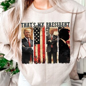 May include: A beige sweatshirt with a graphic print of three men in suits, with the text "THAT'S MY PRESIDENT" above them. The graphic also includes an American flag.
