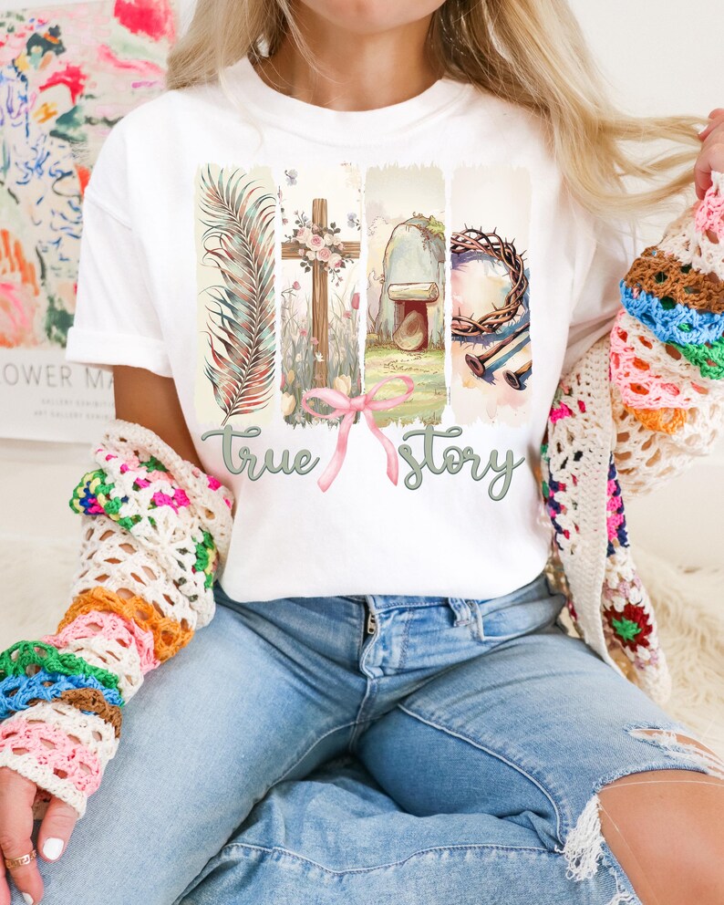 Puede incluir: Camiseta blanca con un dise&ntilde;o gr&aacute;fico de una cruz, una corona de espinas, una piedra, una hoja de palma y las palabras "true story".